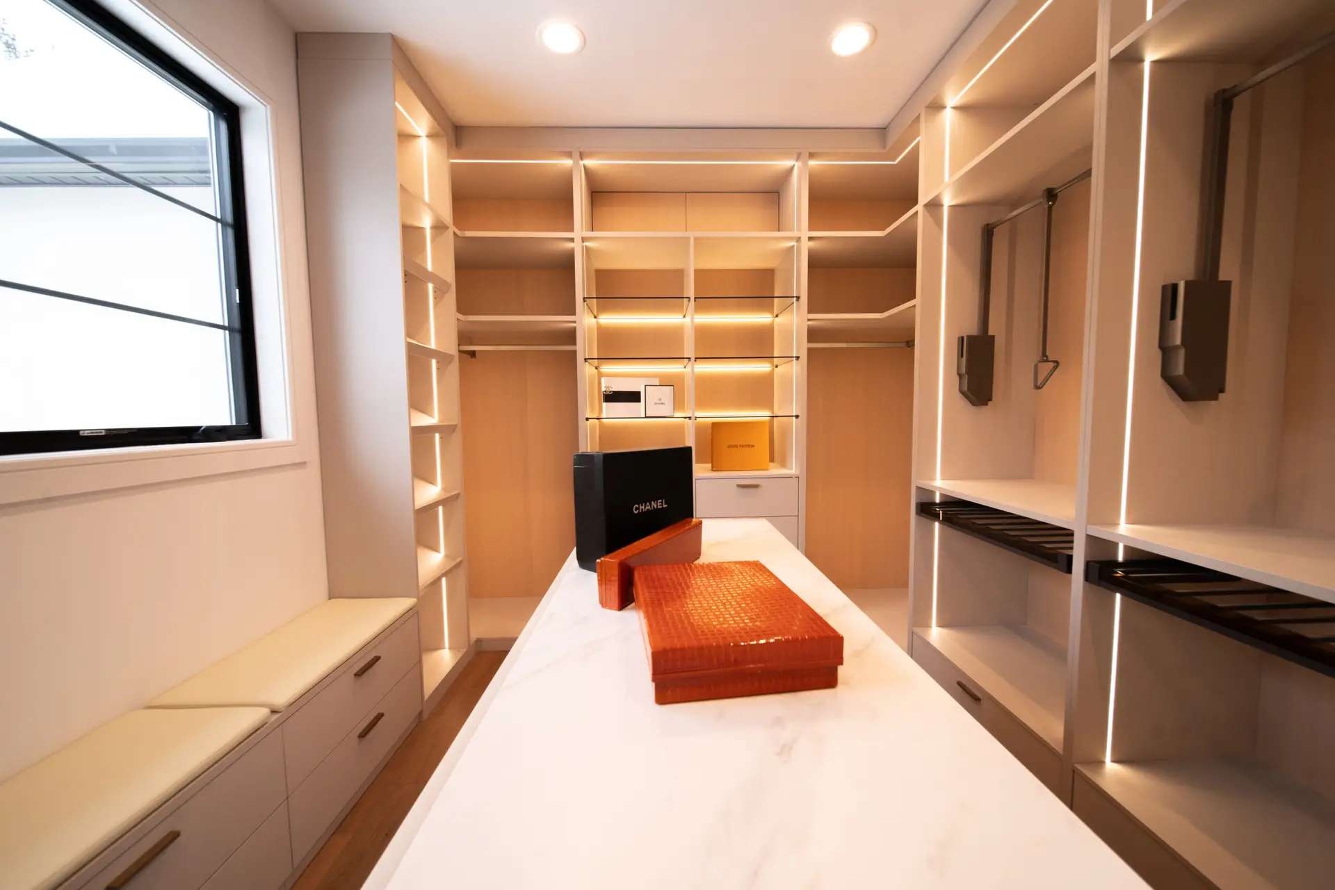 Finished made-in-America custom walk-in closet with premium cabinets, center island, open shelving, hanging space, and bench seating