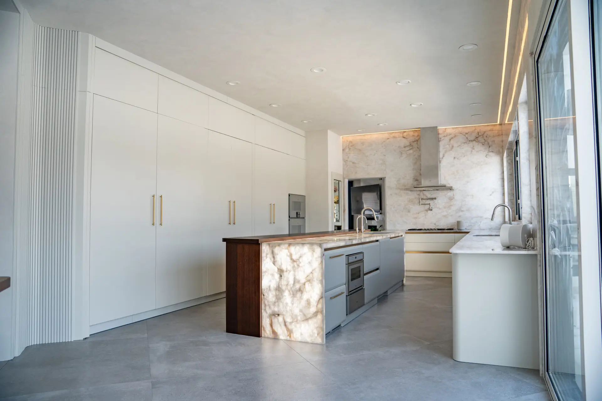 Front angle view of a minimalist custom kitchen with tall cabinets and quartzite finishes by Americana Studio